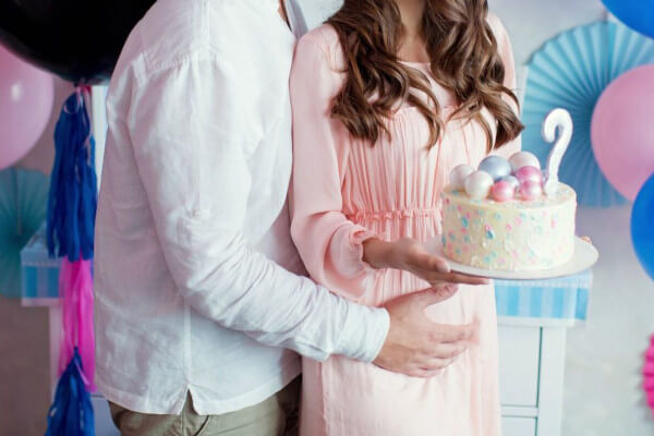 Madre embarazada junto a su pareja en una fiesta de gender reveal con globos y pastel