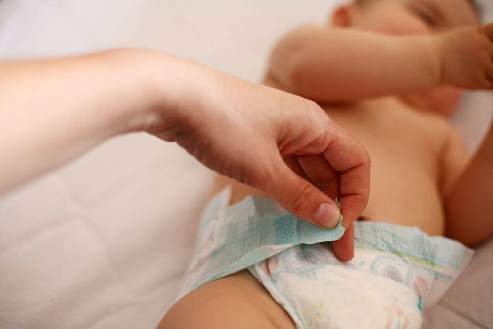 mano pegando la cinta adhesiva del pañal mientras el bebé esta costado en la cama